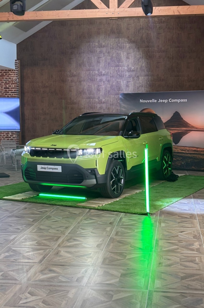 SUV Jeep Compass vert exposé dans un showroom, éclairé par des lumières vertes, avec un panneau en arrière-plan.