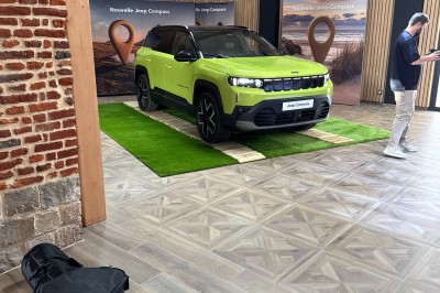 Miniature Location salle Cantin (Nord) - Le Clos du Colombier #25 SUV vert exposé dans une salle avec parquet et murs en bois, accompagné de panneaux promotionnels en arrière-plan.