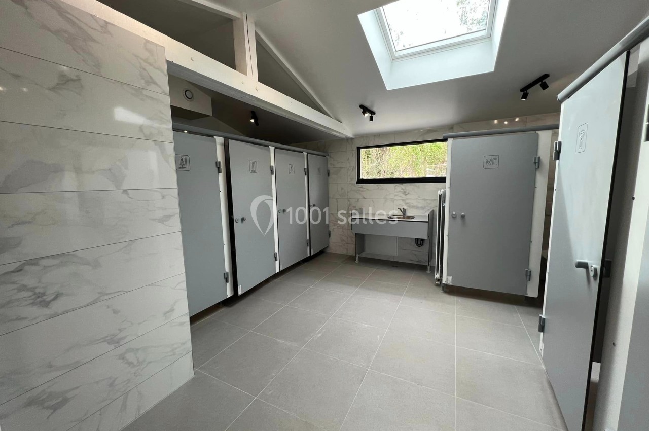 Sanitaires modernes avec cabines fermées, lavabo, murs en carrelage clair et lumière naturelle provenant d'une fenêtre et d…