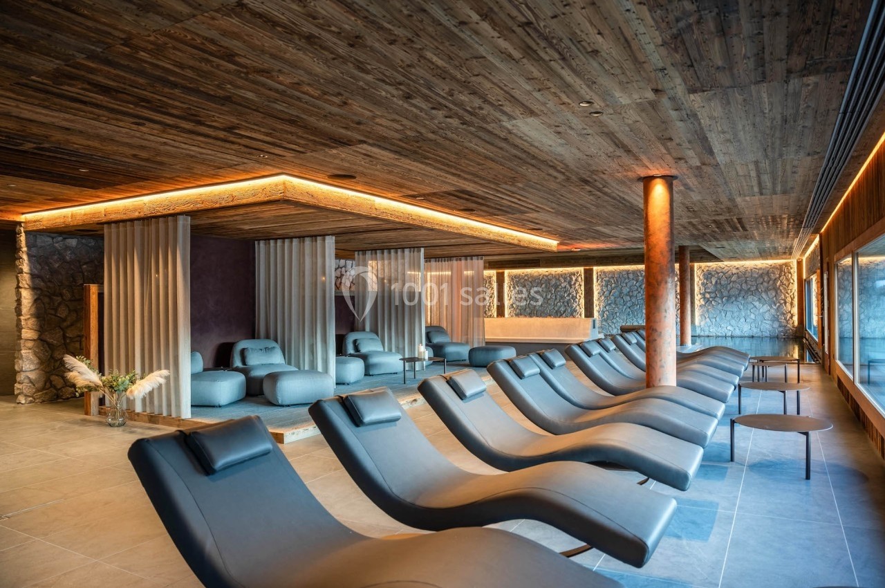Salle de détente avec chaises longues inclinées, éclairage chaleureux et décor en bois et pierre.
