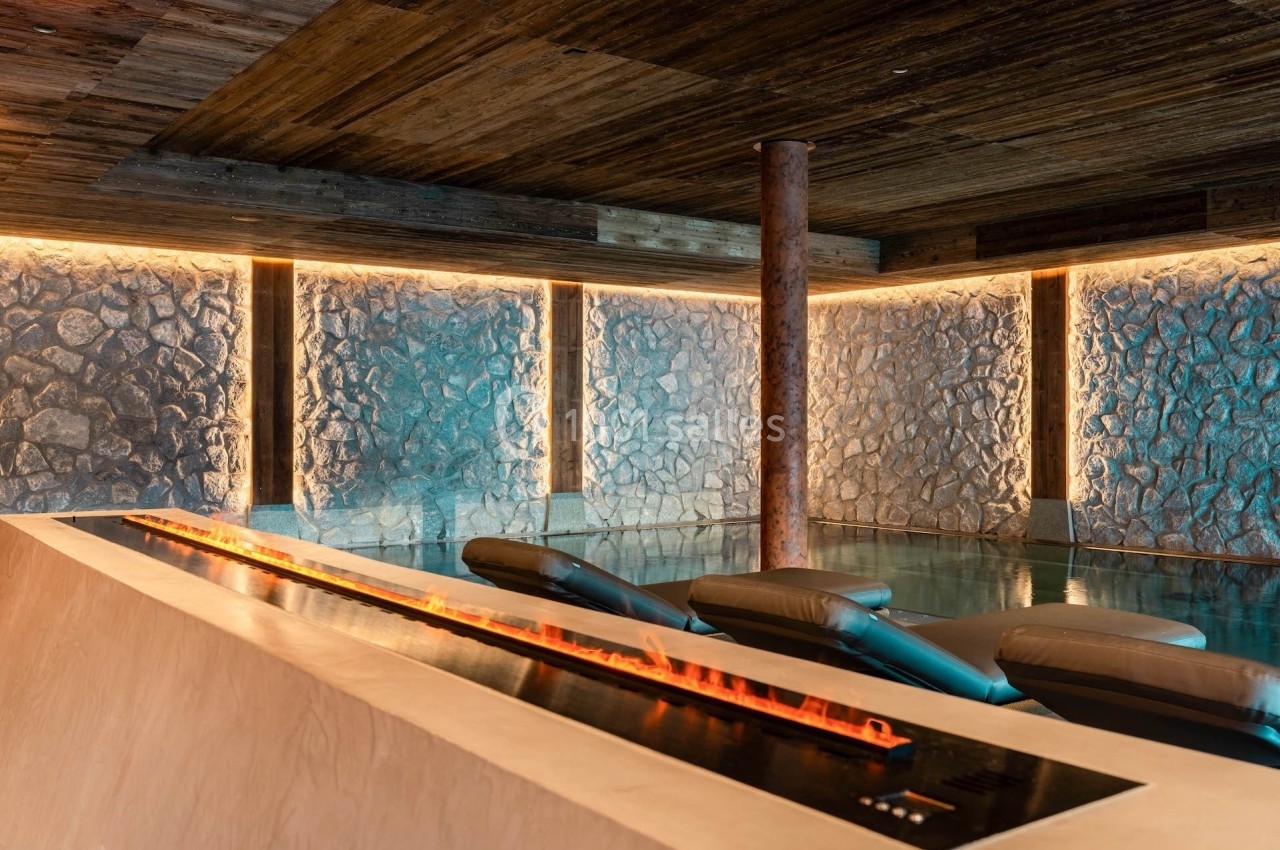 Salle de spa avec chaises longues inclinées, mur en pierre éclairé et cheminée moderne en premier plan.