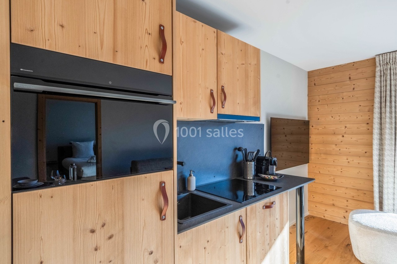 Cuisine moderne en bois avec plaques de cuisson noires, évier intégré et accessoires sur le plan de travail.