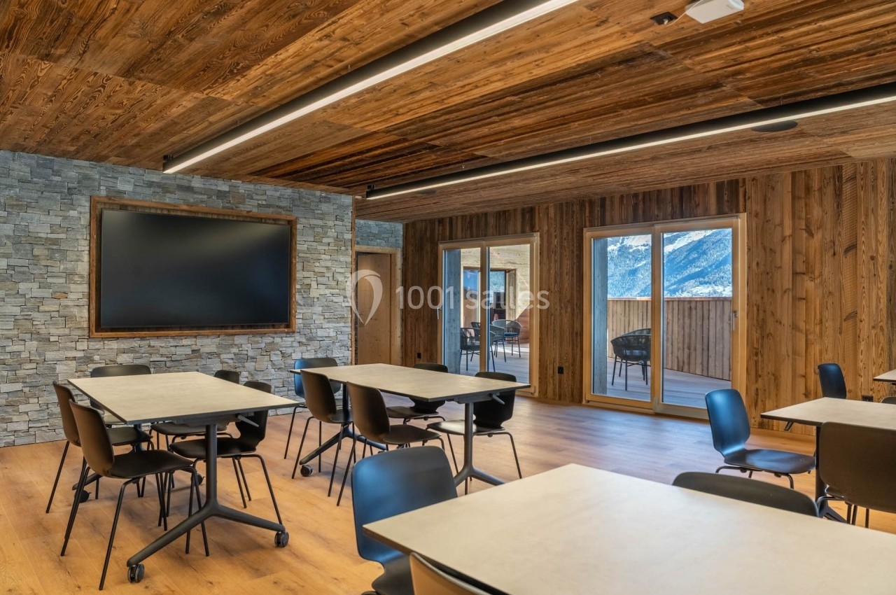 Salle de réunion lumineuse avec murs en bois et pierre, tables et chaises modernes, vue sur les montagnes par les fenêtres.