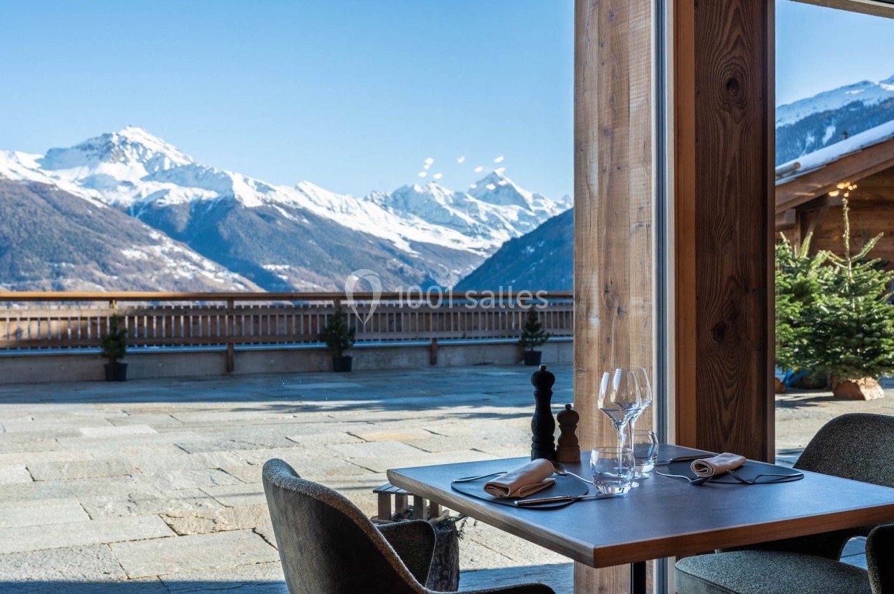 Table dressée près d'une baie vitrée avec vue sur des montagnes enneigées et une terrasse ensoleillée.
