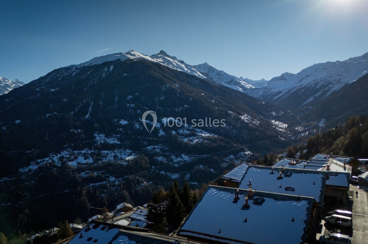 Vue aérienne d'un village de montagne enneigé entouré de sommets alpins sous un ciel dégagé.