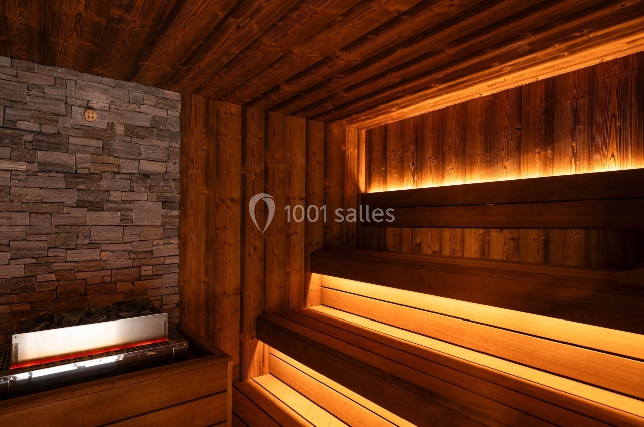 Intérieur d'un sauna en bois avec bancs éclairés et mur en pierre, créant une ambiance chaleureuse.