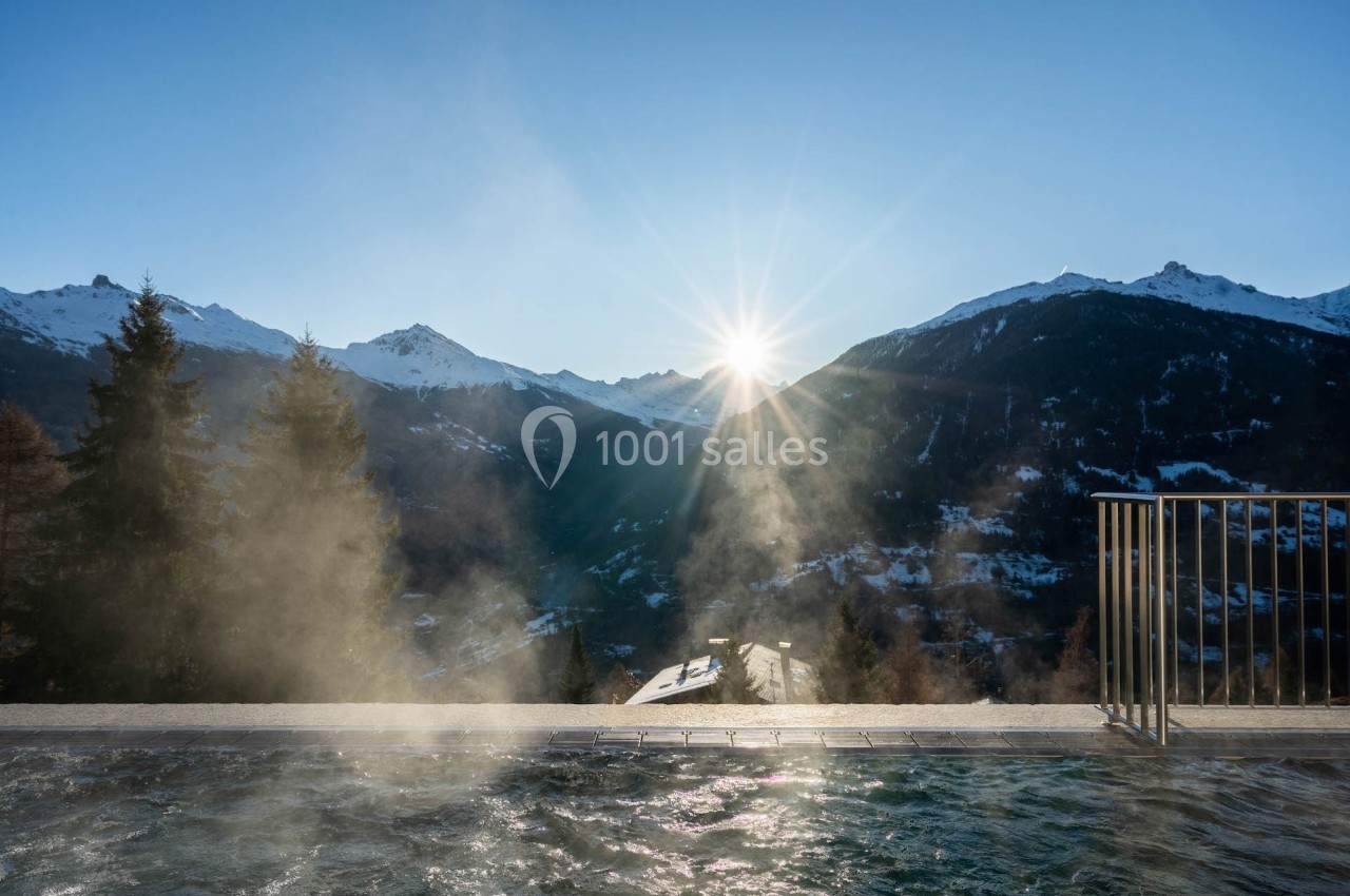 Vue sur des montagnes enneigées au lever du soleil depuis une piscine extérieure dégageant de la vapeur.