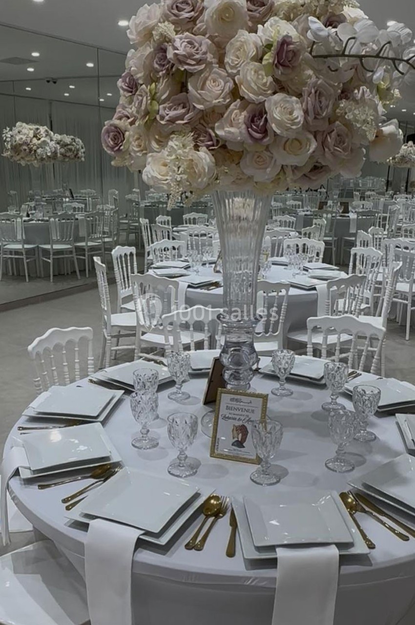 Centre de table floral élégant avec roses pastel sur une table dressée avec vaisselle blanche et couverts dorés.