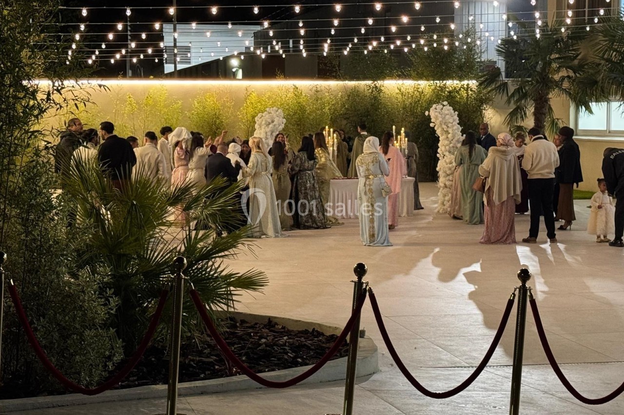 Groupe de personnes en tenue élégante rassemblées dans un espace extérieur décoré de guirlandes lumineuses.