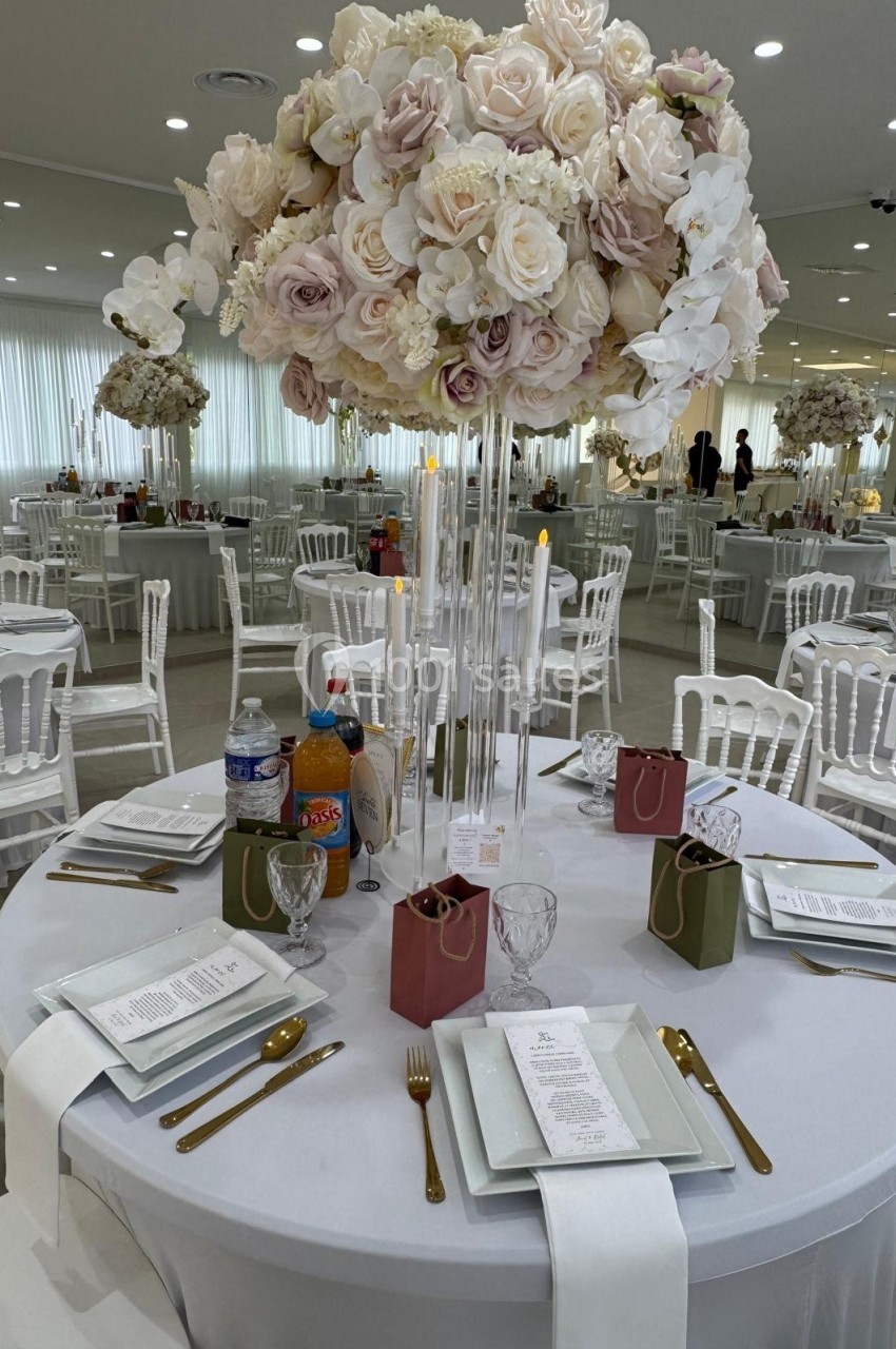 Centre de table floral avec roses et orchidées blanches, entouré de couverts dorés et menus sur une table dressée.