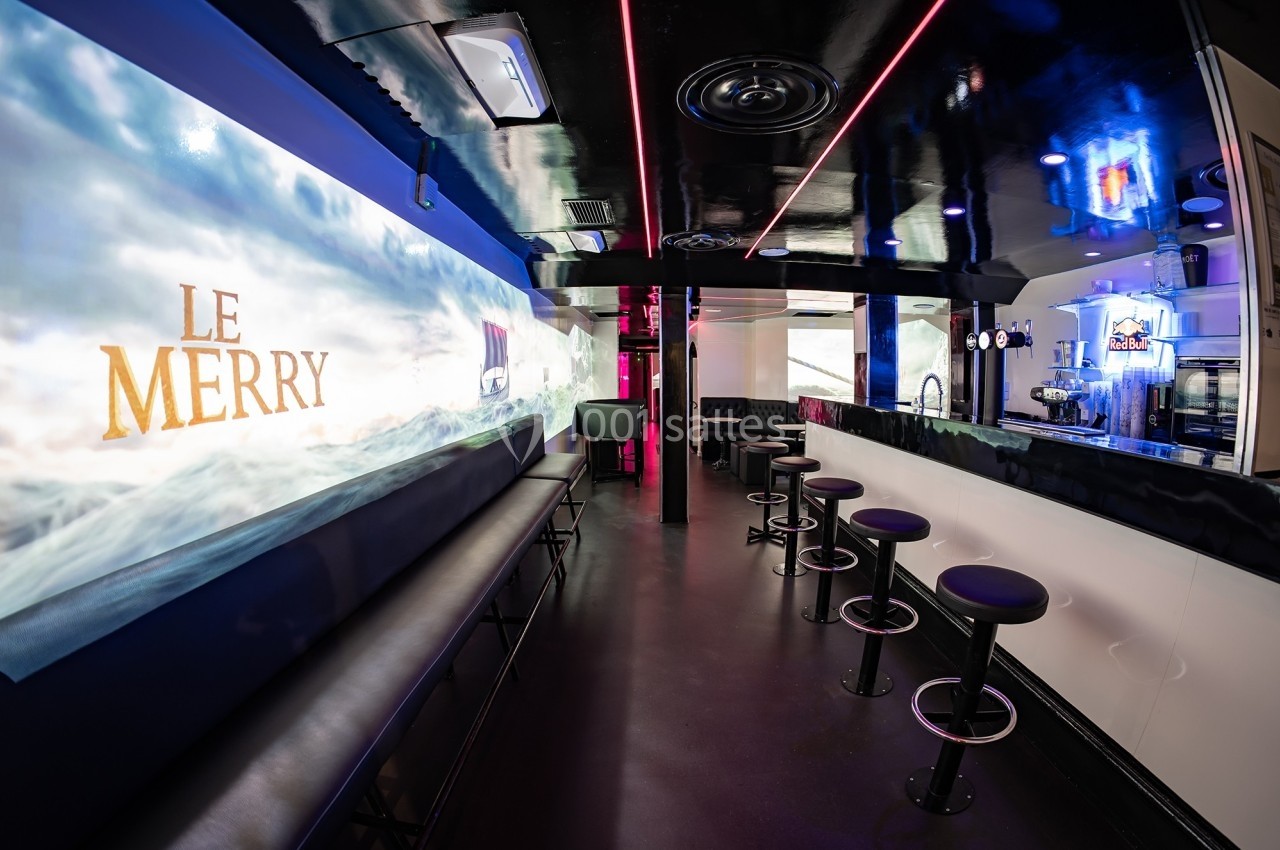 Intérieur d'un bar moderne avec comptoir, tabourets hauts, banquettes noires et éclairage néon coloré.