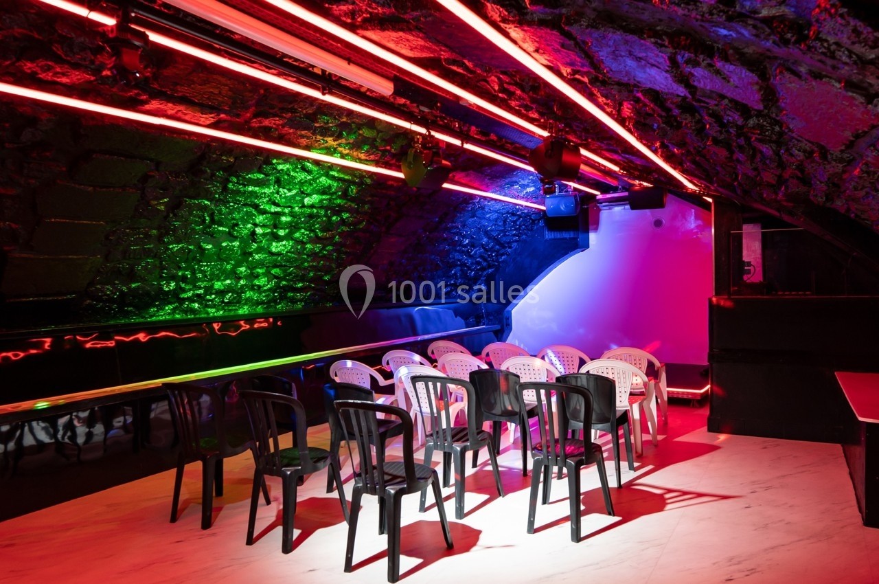 Salle voûtée avec des chaises en plastique disposées face à un mur éclairé par des néons rouges et verts.