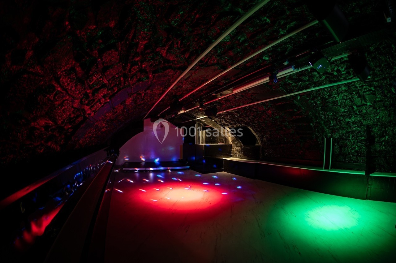 Salle voûtée avec éclairage coloré rouge et vert, sol en marbre et ambiance de club nocturne.