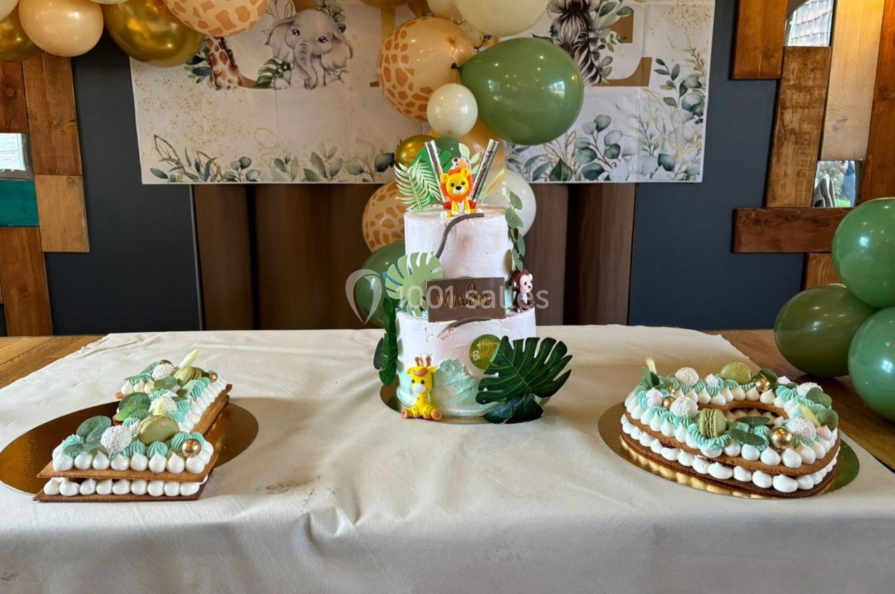 Gâteau à étages décoré sur le thème de la jungle, entouré de desserts et de ballons assortis.