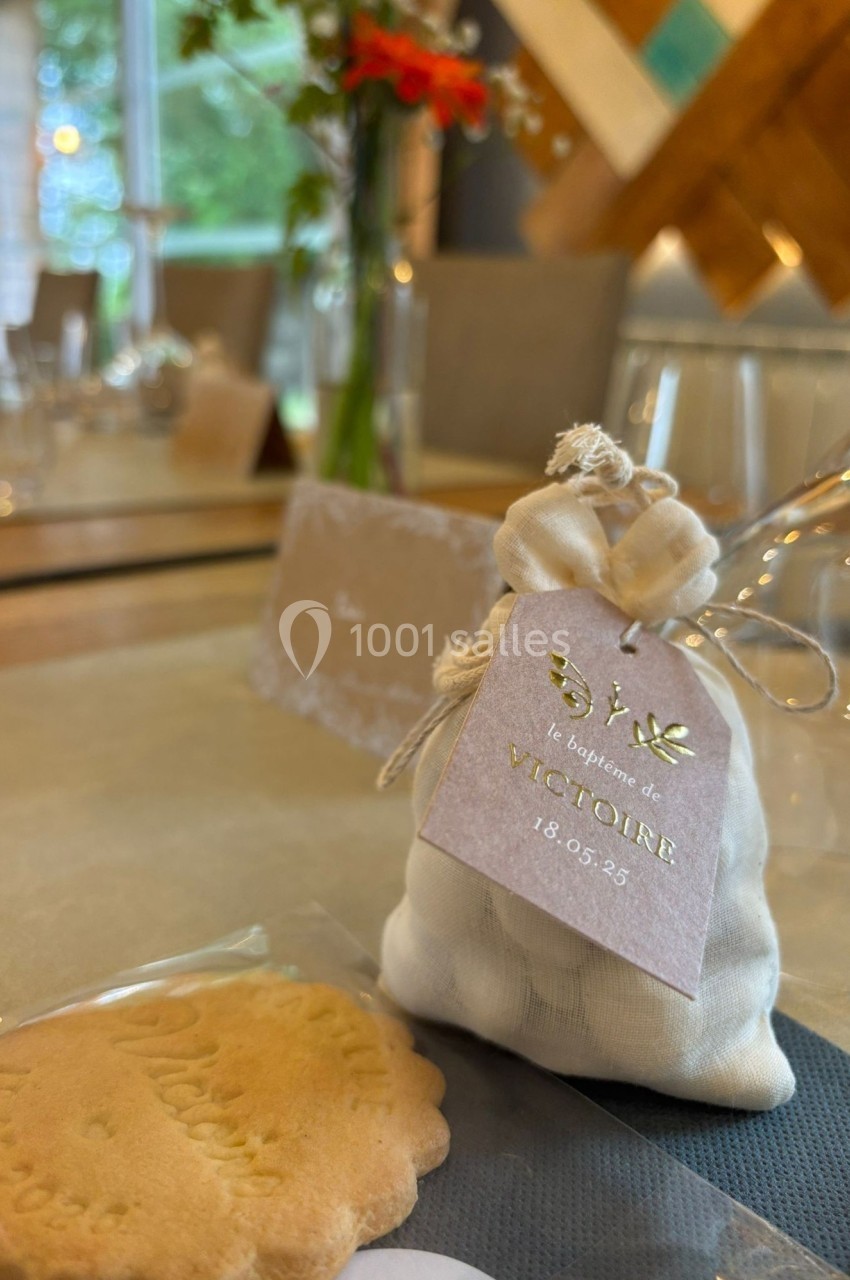 Petit sachet personnalisé pour un baptême, posé sur une table décorée avec des fleurs et des biscuits.