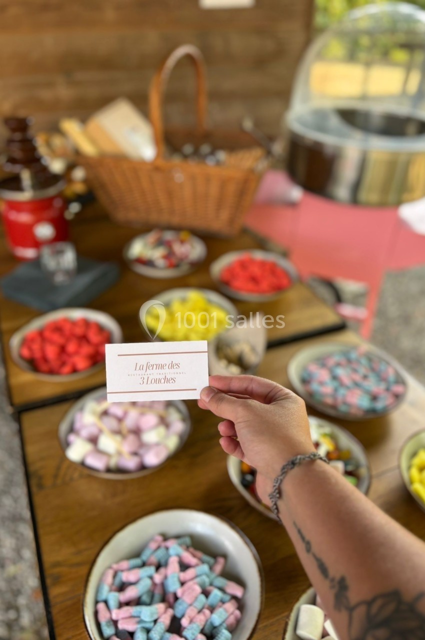 Une main tient une étiquette devant une table garnie de bonbons colorés, de fruits et d'une fontaine à chocolat.