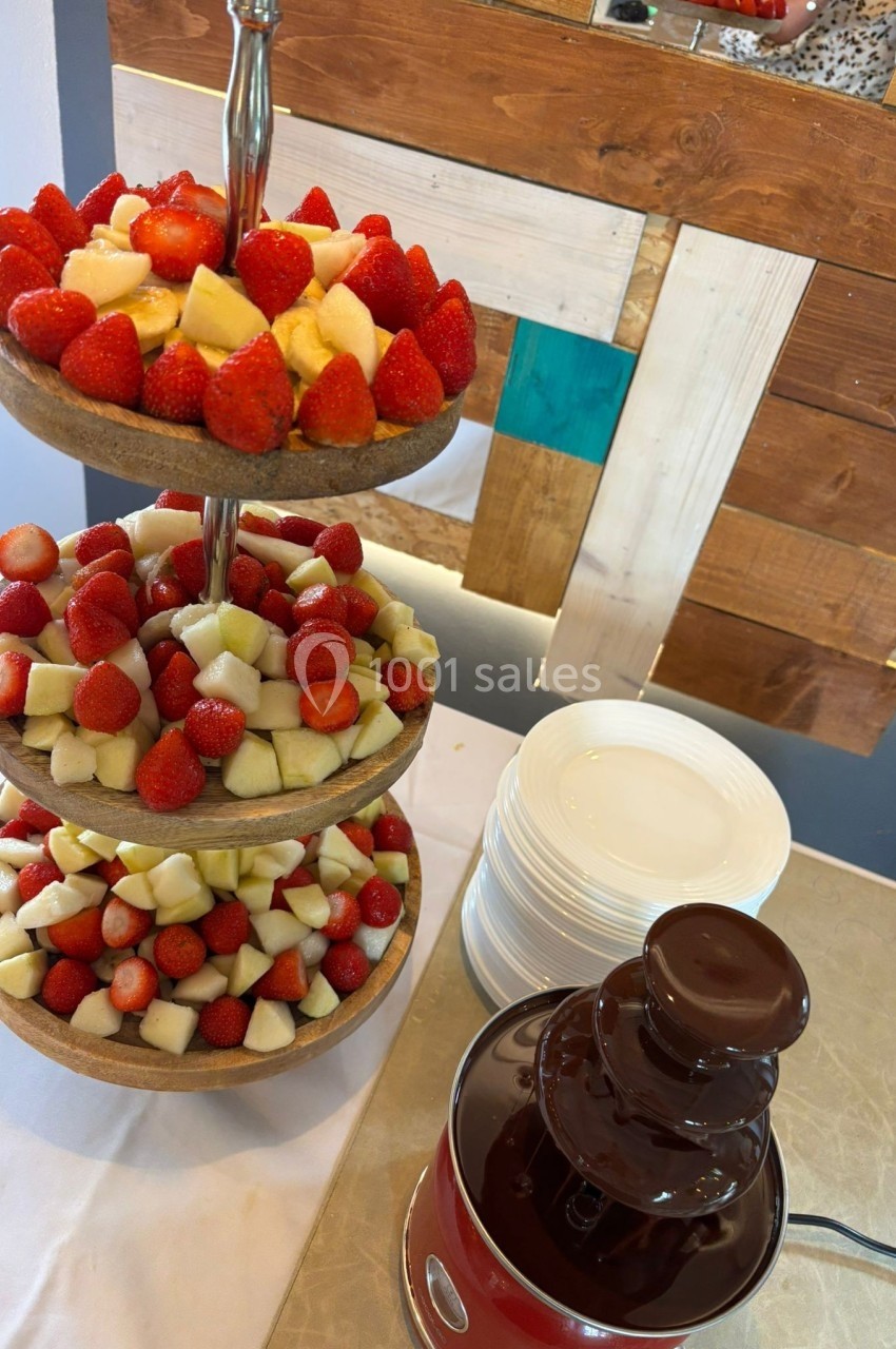 Plateau à trois étages avec fraises et morceaux de fruits, accompagné d'une fontaine de chocolat sur une table.