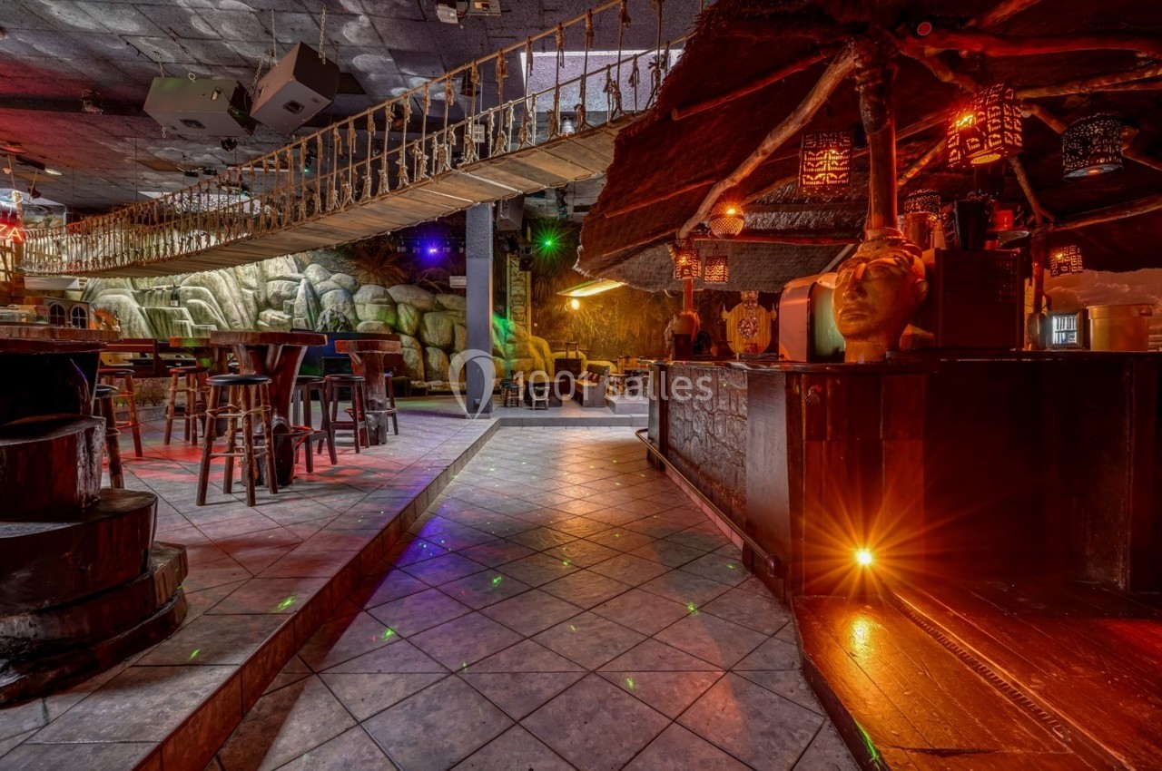 Intérieur d'un bar à thème exotique avec pont suspendu, éclairage coloré et décorations tropicales.