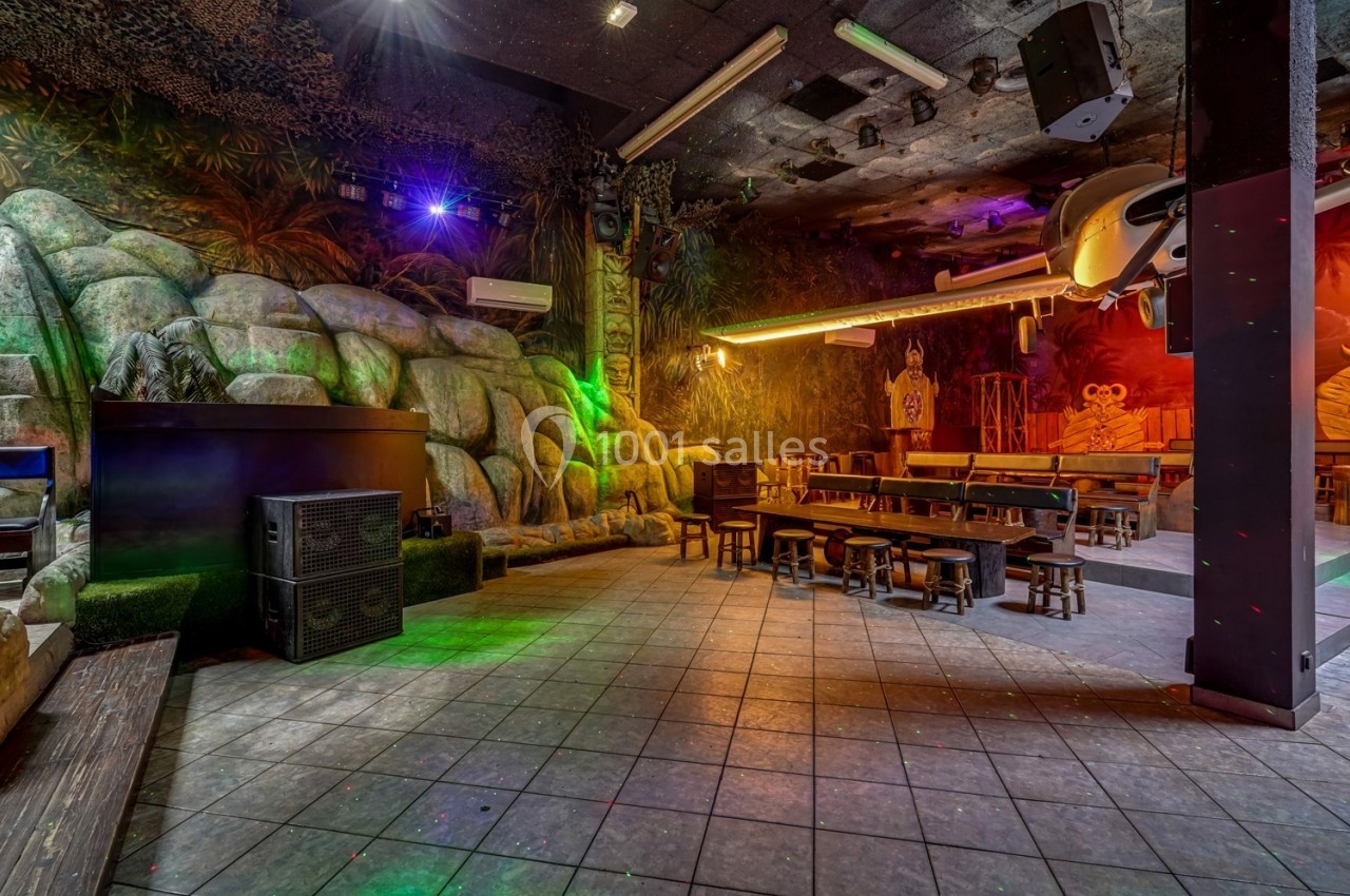 Salle thématique avec décor tropical, bancs en bois, éclairage coloré et éléments de jungle en arrière-plan.