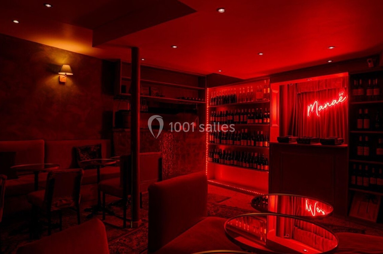 Salle de bar tamisée avec éclairage rouge, étagères remplies de bouteilles et enseigne lumineuse ’Maria’.