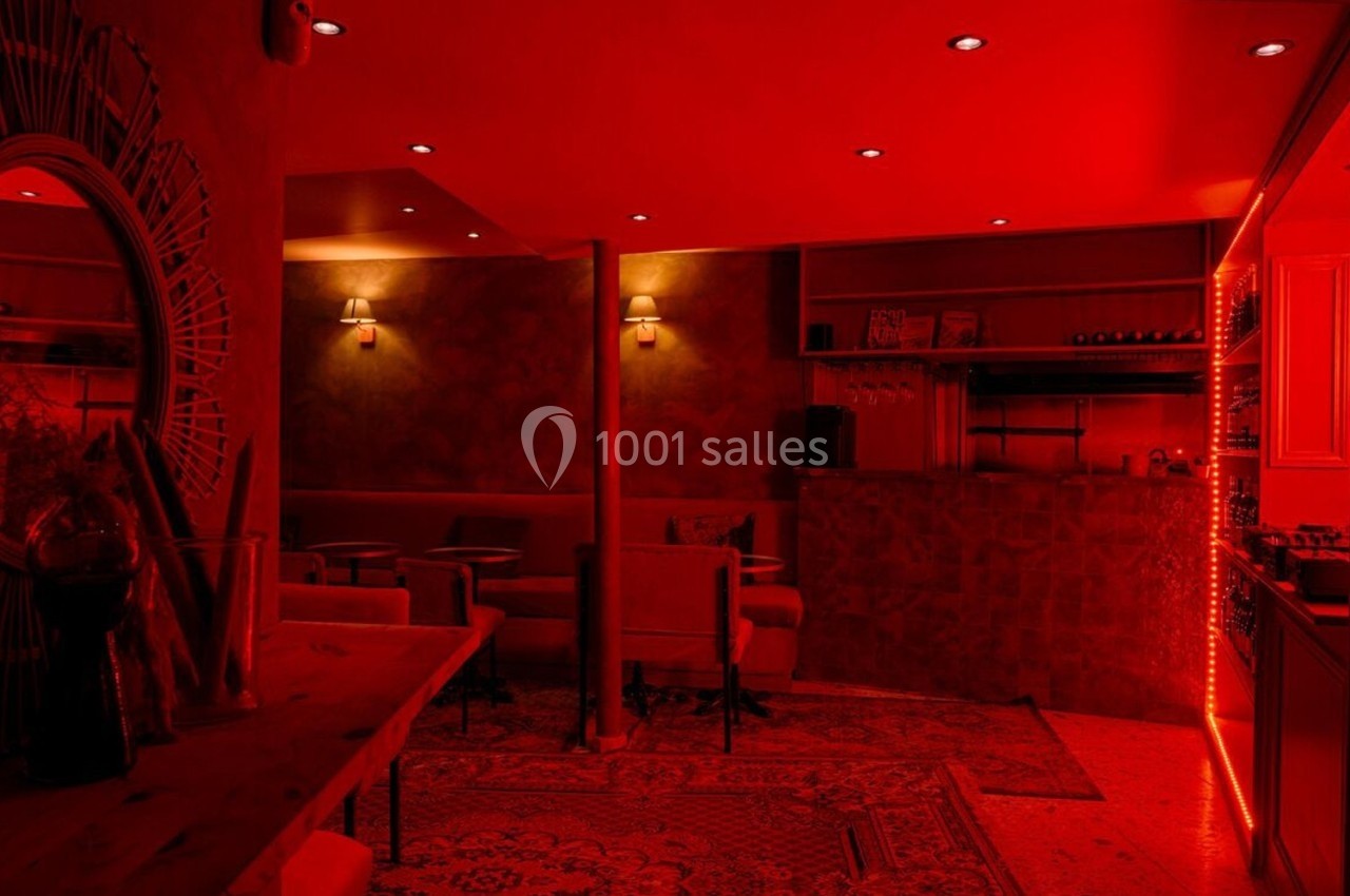 Salle de bar à l'éclairage rouge tamisé, avec mobilier confortable, étagères de bouteilles et décoration chaleureuse.