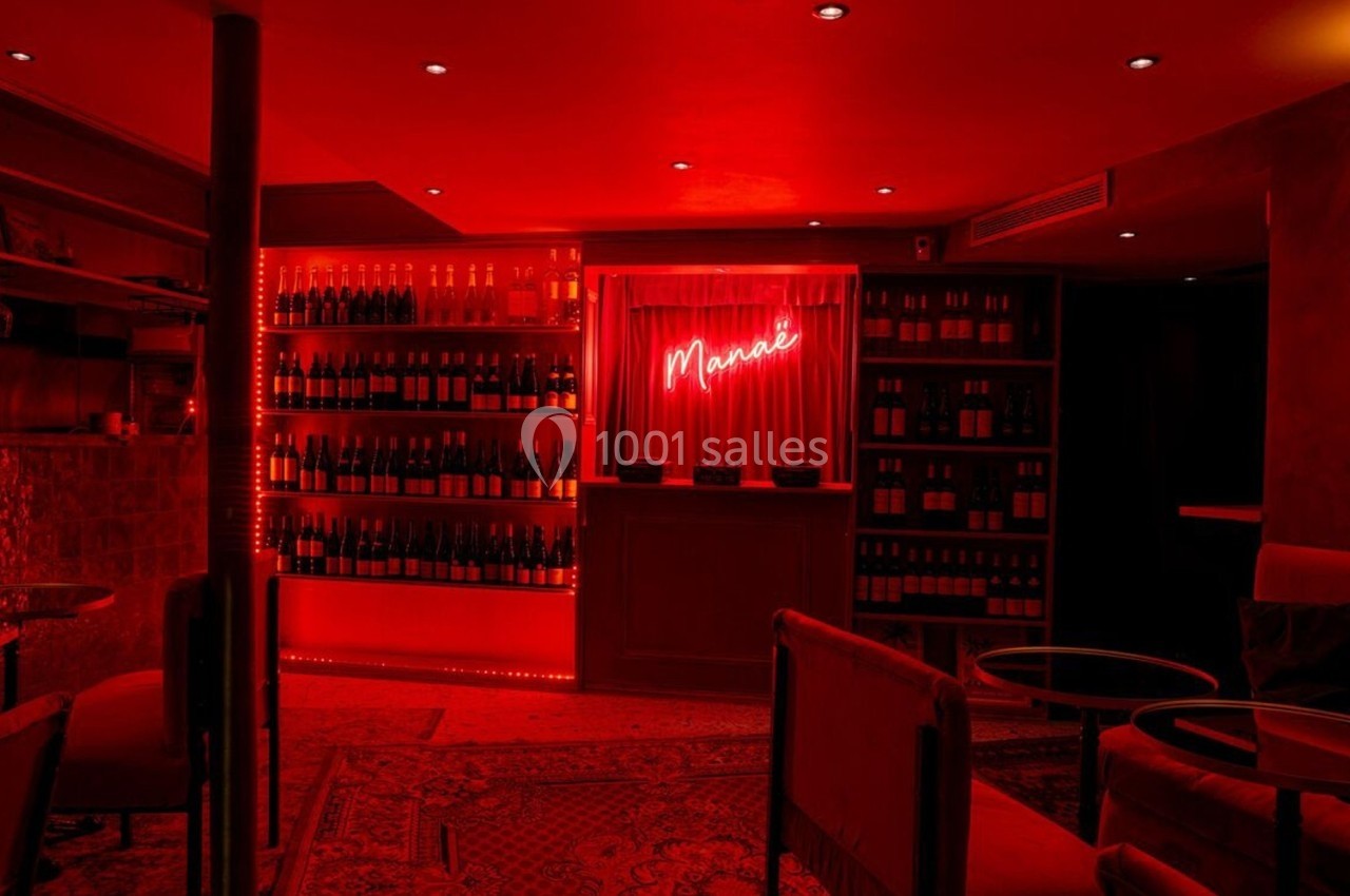 Bar à l'éclairage rouge tamisé avec étagères de bouteilles, tables basses et fauteuils dans une ambiance chaleureuse.