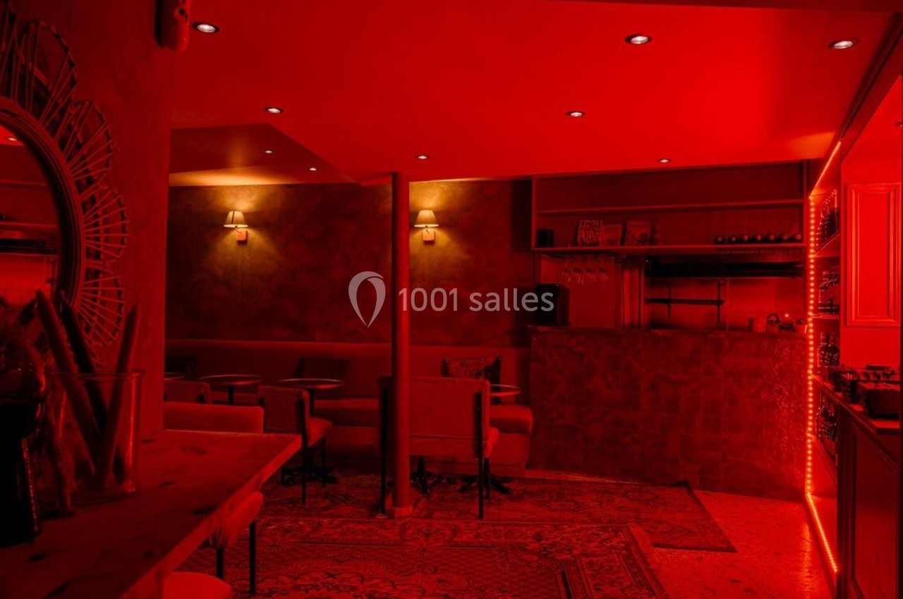 Salle de bar à l'éclairage rouge tamisé, avec des tables, des chaises et des étagères de bouteilles de vin.