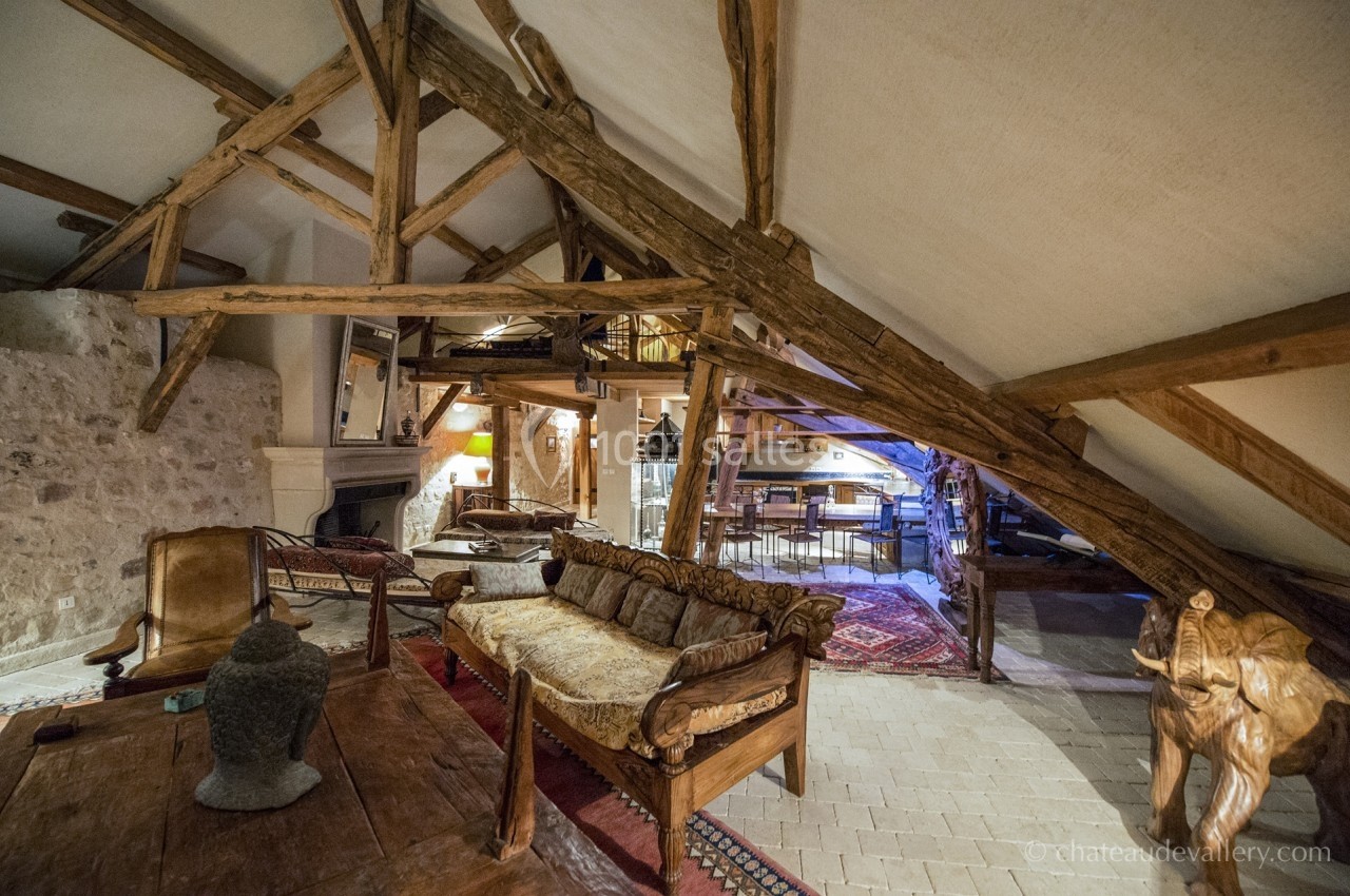 Salon rustique avec poutres apparentes, mobilier en bois, cheminée en pierre et éclairage chaleureux.