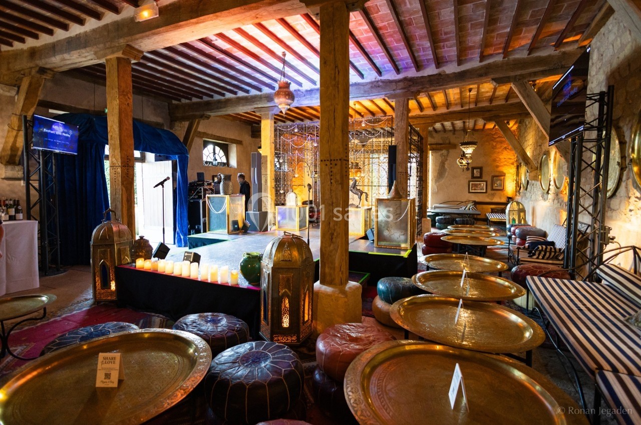 Salle décorée dans un style oriental avec des tables basses dorées, des poufs colorés et une scène éclairée.