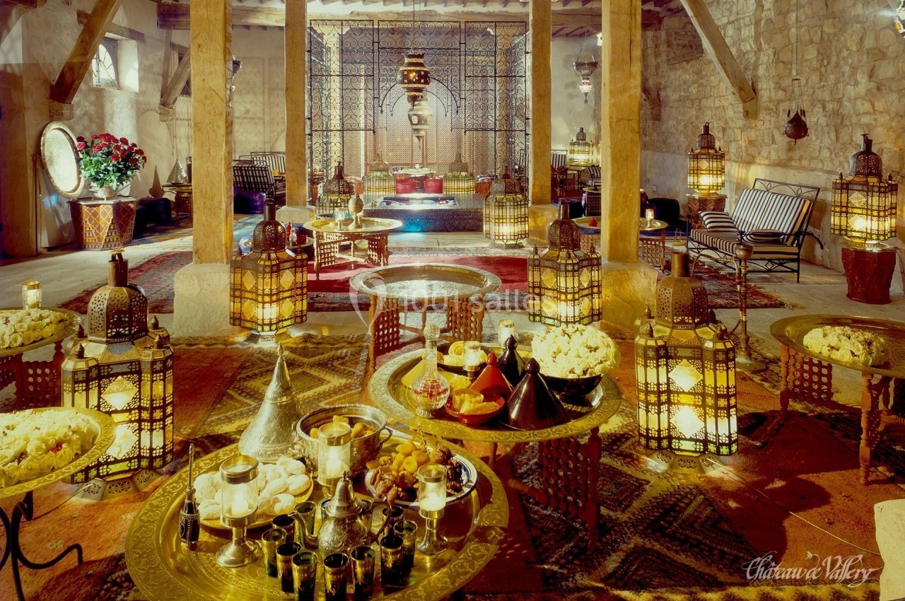Salle décorée dans un style oriental avec lanternes, tapis, tables basses et plats traditionnels disposés au premier plan.
