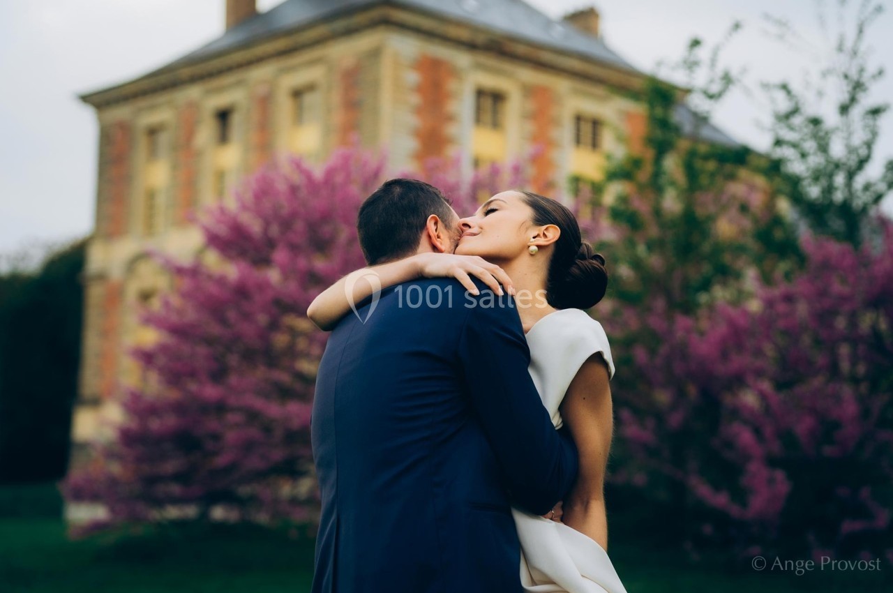 Un couple s'enlace tendrement devant un bâtiment ancien et des arbres en fleurs.