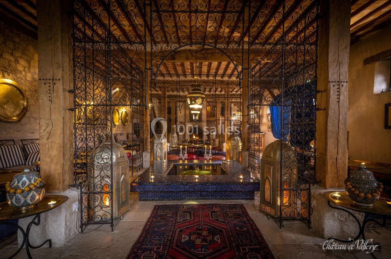 Salle décorée dans un style oriental avec des lanternes, un bassin central et des motifs traditionnels.