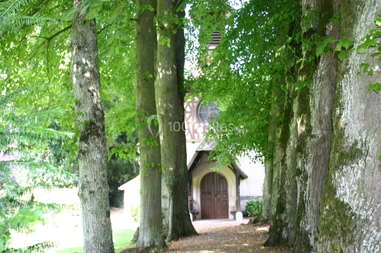 Allée bordée d'arbres menant à une petite chapelle avec une porte en bois et un toit en pente.