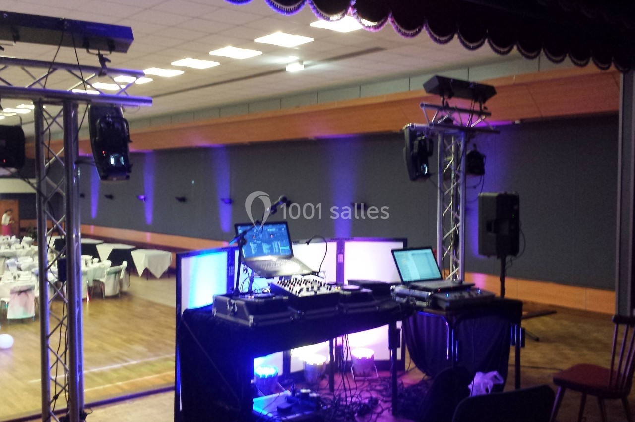 Équipement de DJ installé dans une salle de réception avec tables dressées et éclairage coloré.