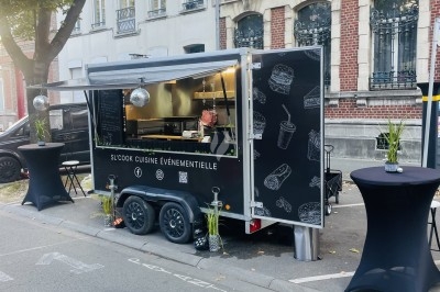 Burger au saumon fumé avec laitue, tomate et sauce, posé sur une table en marbre avec citron vert et herbes en arrière-plan.