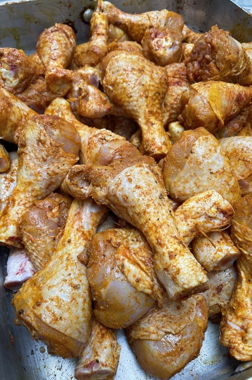 Pilons de poulet marinés avec des épices, disposés dans un plat en métal avant cuisson.