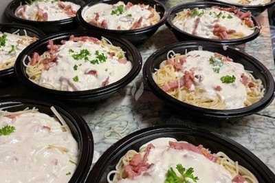 Burger au saumon fumé avec laitue, tomate et sauce, posé sur une table en marbre avec citron vert et herbes en arrière-plan.