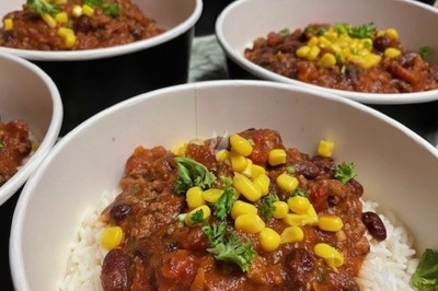 Burger au saumon fumé avec laitue, tomate et sauce, posé sur une table en marbre avec citron vert et herbes en arrière-plan.
