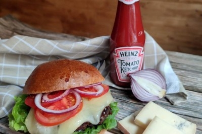 Burger au saumon fumé avec laitue, tomate et sauce, posé sur une table en marbre avec citron vert et herbes en arrière-plan.
