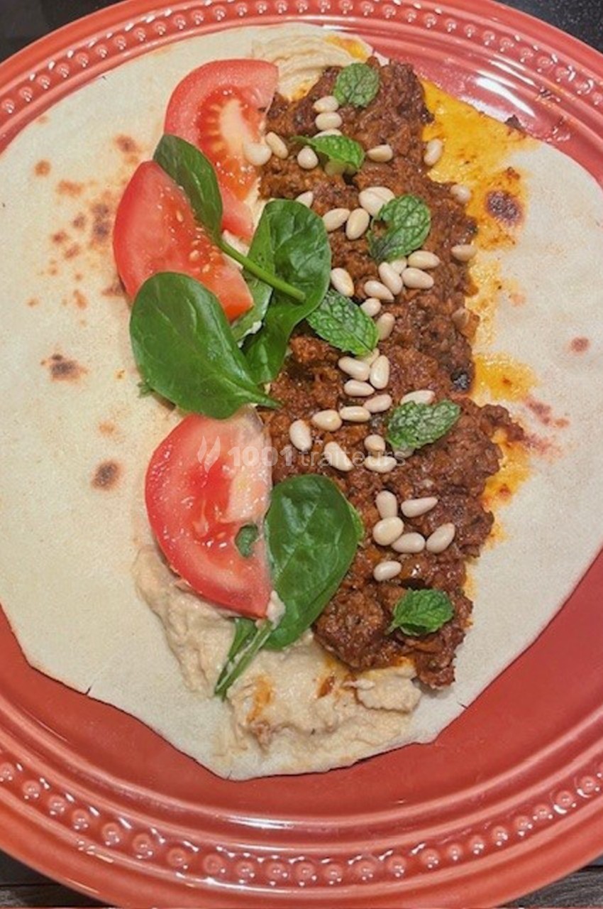 Wrap ouvert garni de viande épicée, houmous, tranches de tomate, feuilles d'épinard, pignons et menthe, sur une assiette…