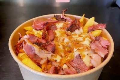 Burger au saumon fumé avec laitue, tomate et sauce, posé sur une table en marbre avec citron vert et herbes en arrière-plan.