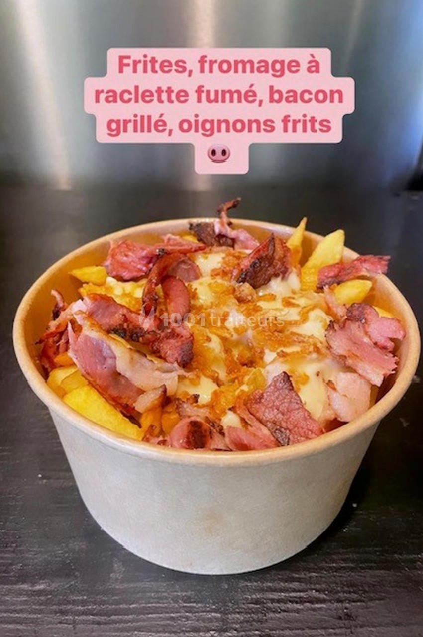 Bol de frites garnies de fromage à raclette fumé, bacon grillé et oignons frits, posé sur une surface noire.