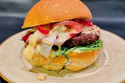 Burger au saumon fumé avec laitue, tomate et sauce, posé sur une table en marbre avec citron vert et herbes en arrière-plan.