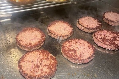 Burger au saumon fumé avec laitue, tomate et sauce, posé sur une table en marbre avec citron vert et herbes en arrière-plan.