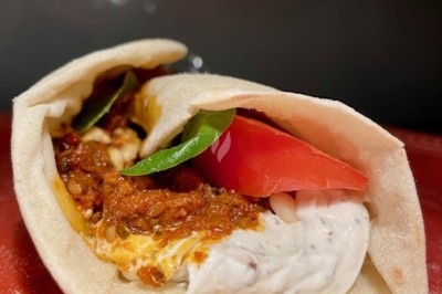 Burger au saumon fumé avec laitue, tomate et sauce, posé sur une table en marbre avec citron vert et herbes en arrière-plan.