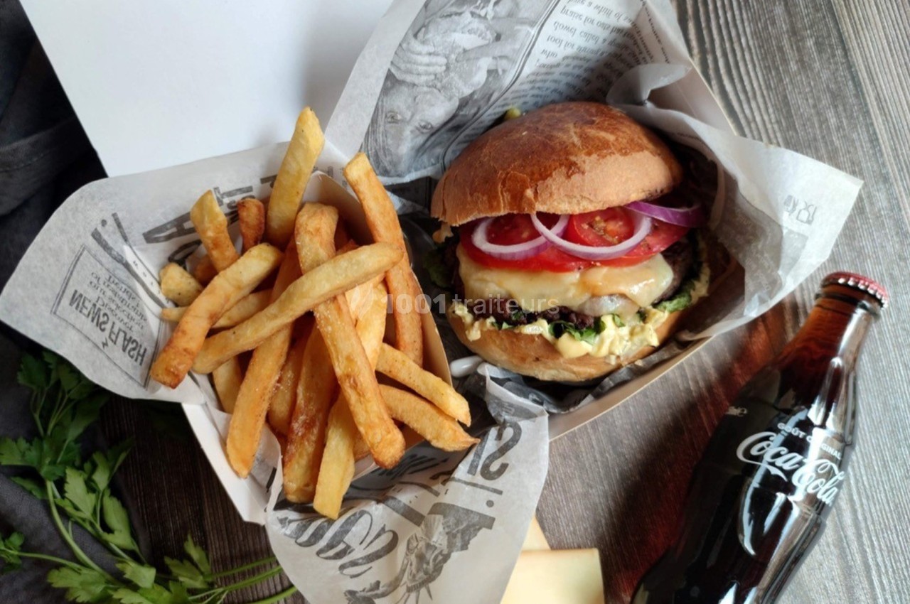 Burger garni de légumes et fromage, accompagné de frites et d'une bouteille de Coca-Cola, sur une table en bois.
