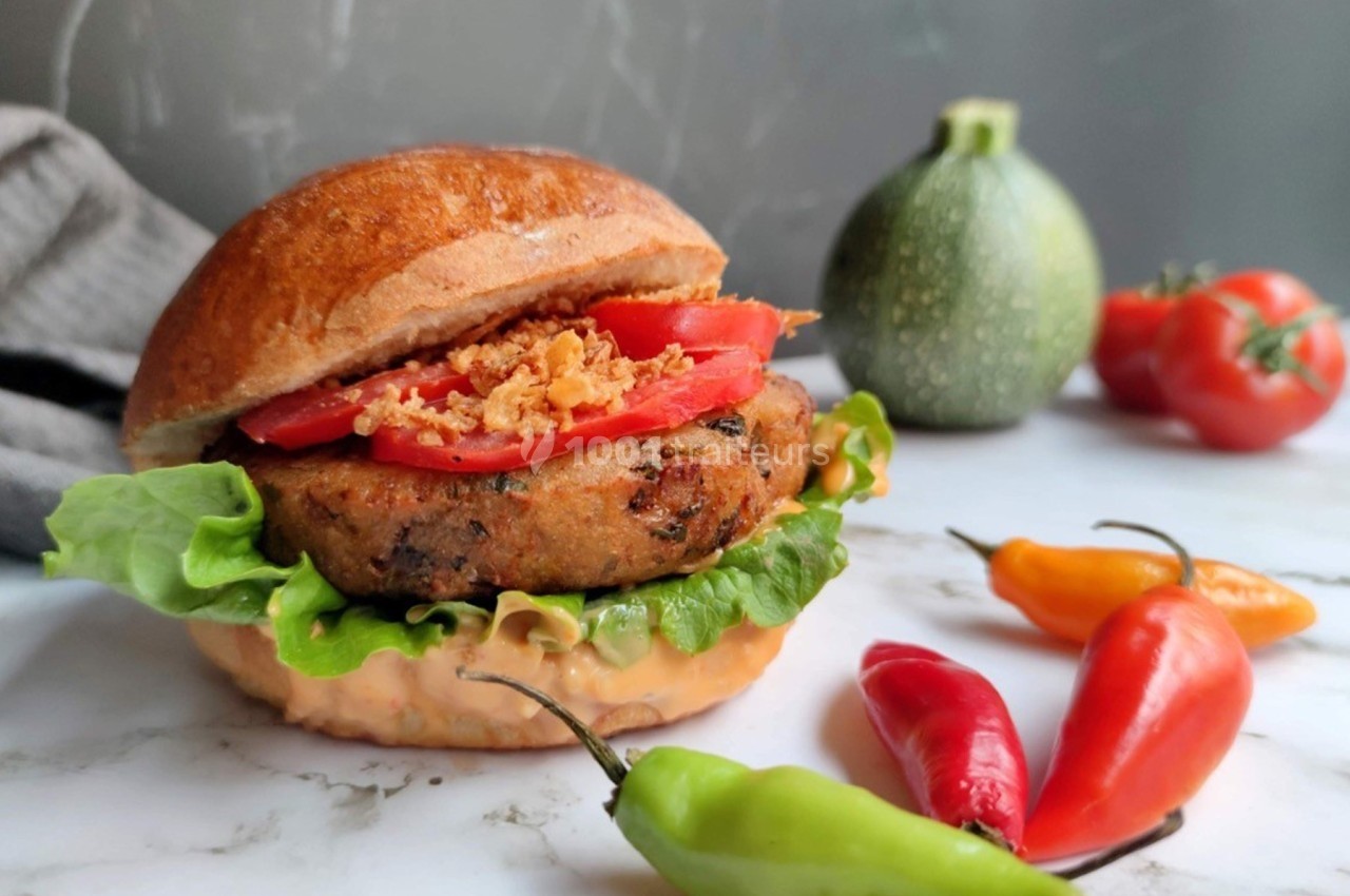 Burger végétarien garni de salade, tomate et oignons frits, avec des piments et une courgette en arrière-plan.