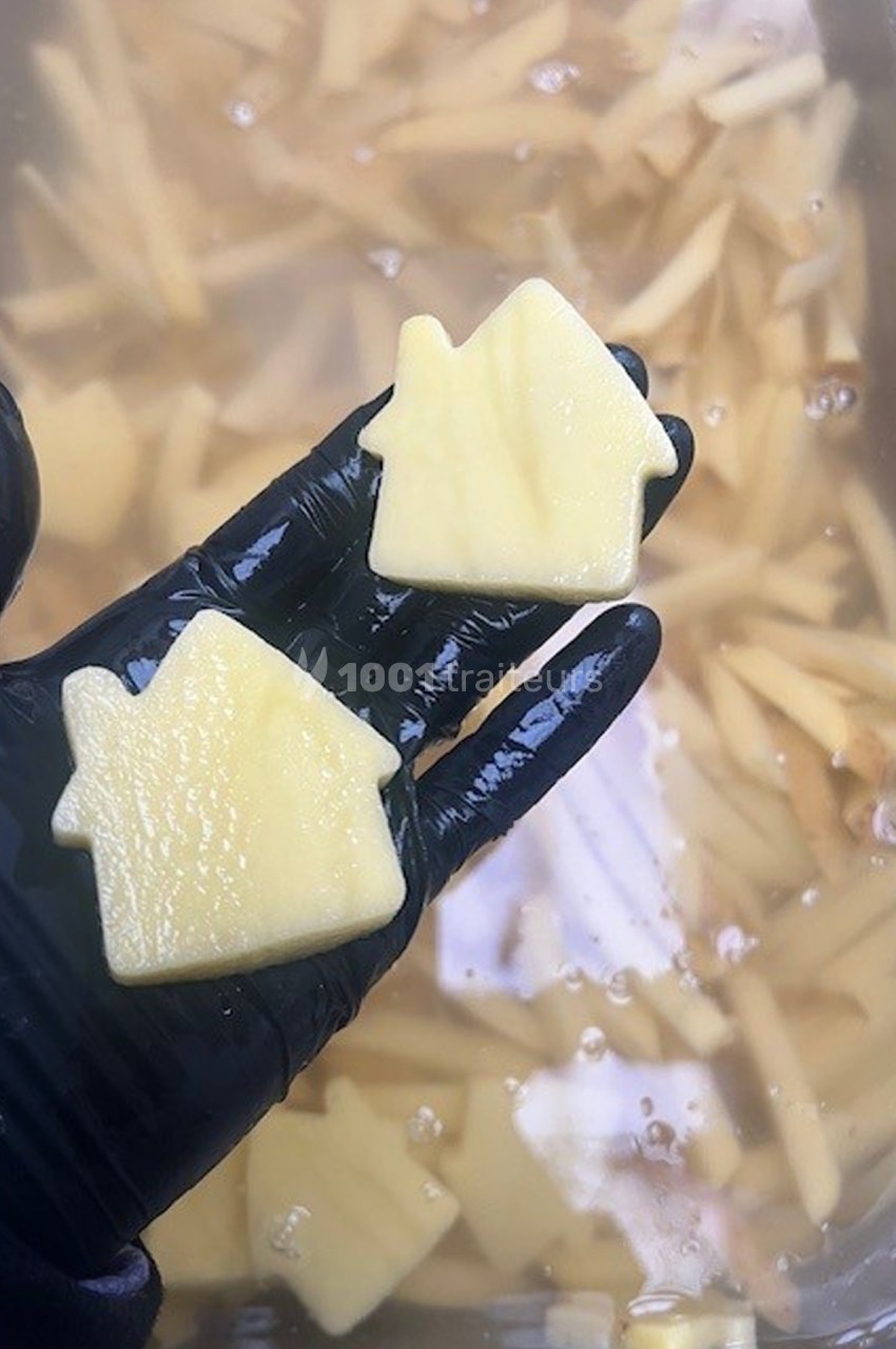 Deux morceaux de pommes de terre découpés en forme de maison, tenus par une main gantée au-dessus d'eau.