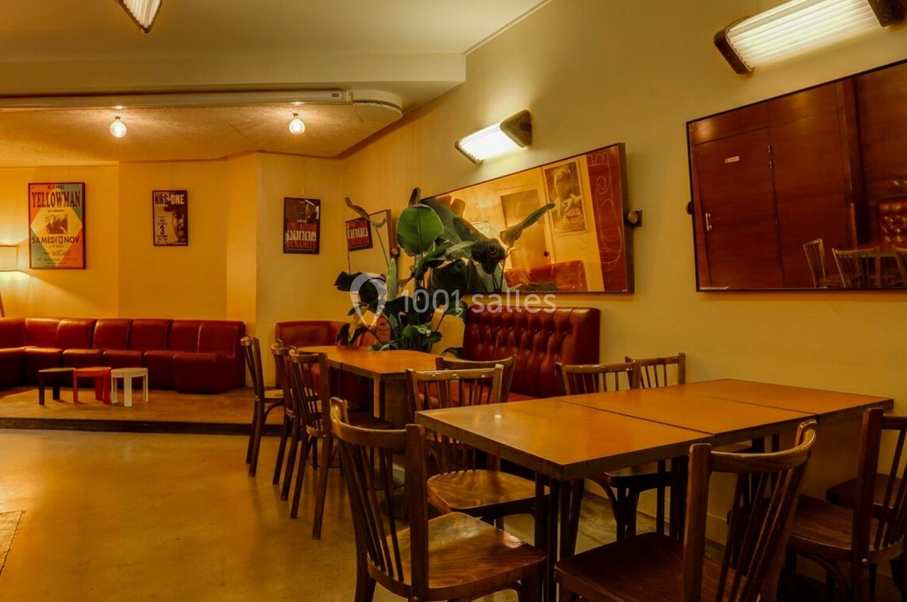 Salle chaleureuse avec tables en bois, chaises assorties, banquettes rouges et affiches rétro sur les murs.