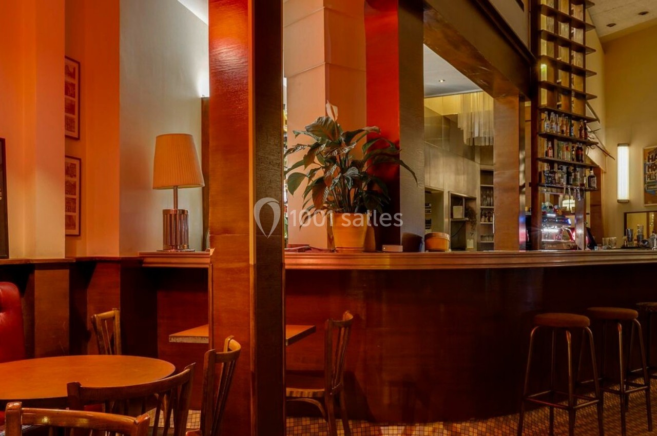 Intérieur d'un café-bar chaleureux avec des tabourets, des tables en bois et une lumière tamisée.